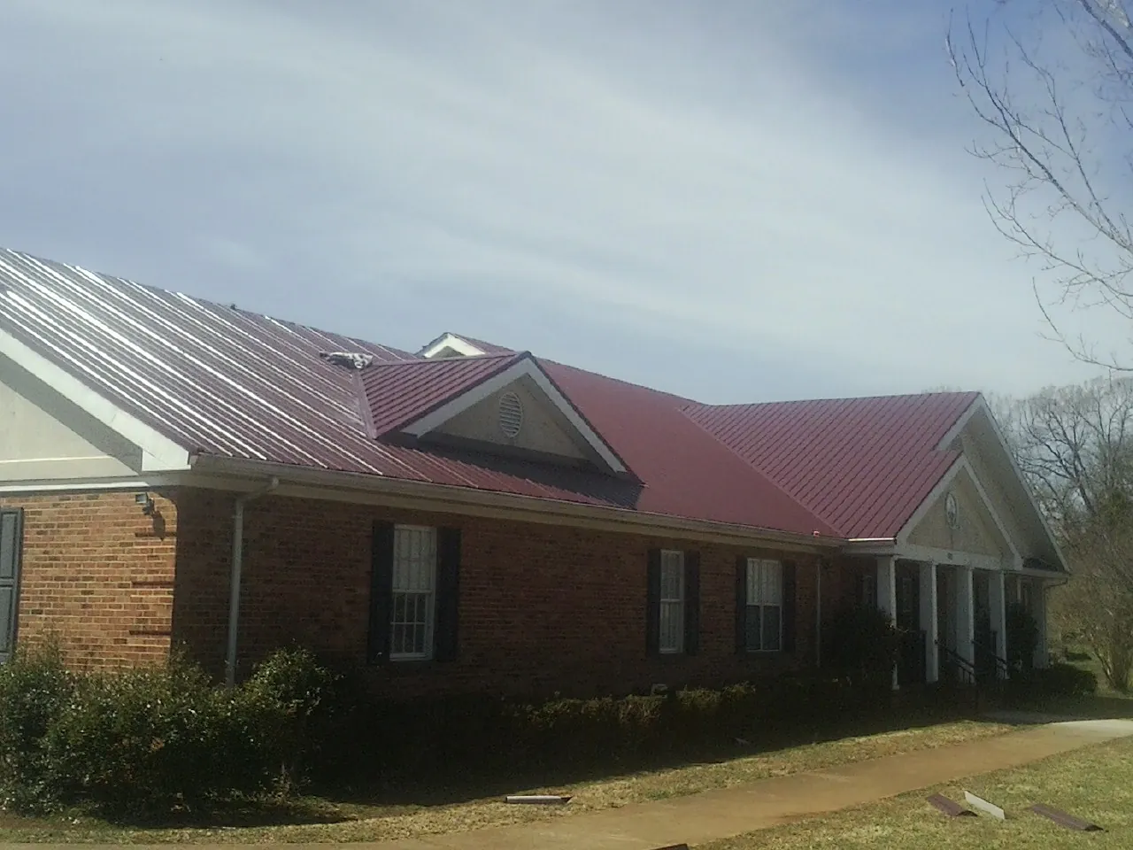 Red metal roof with gabled entries on a long brick building, from a Hail Damage Roof Repair job in Yerington