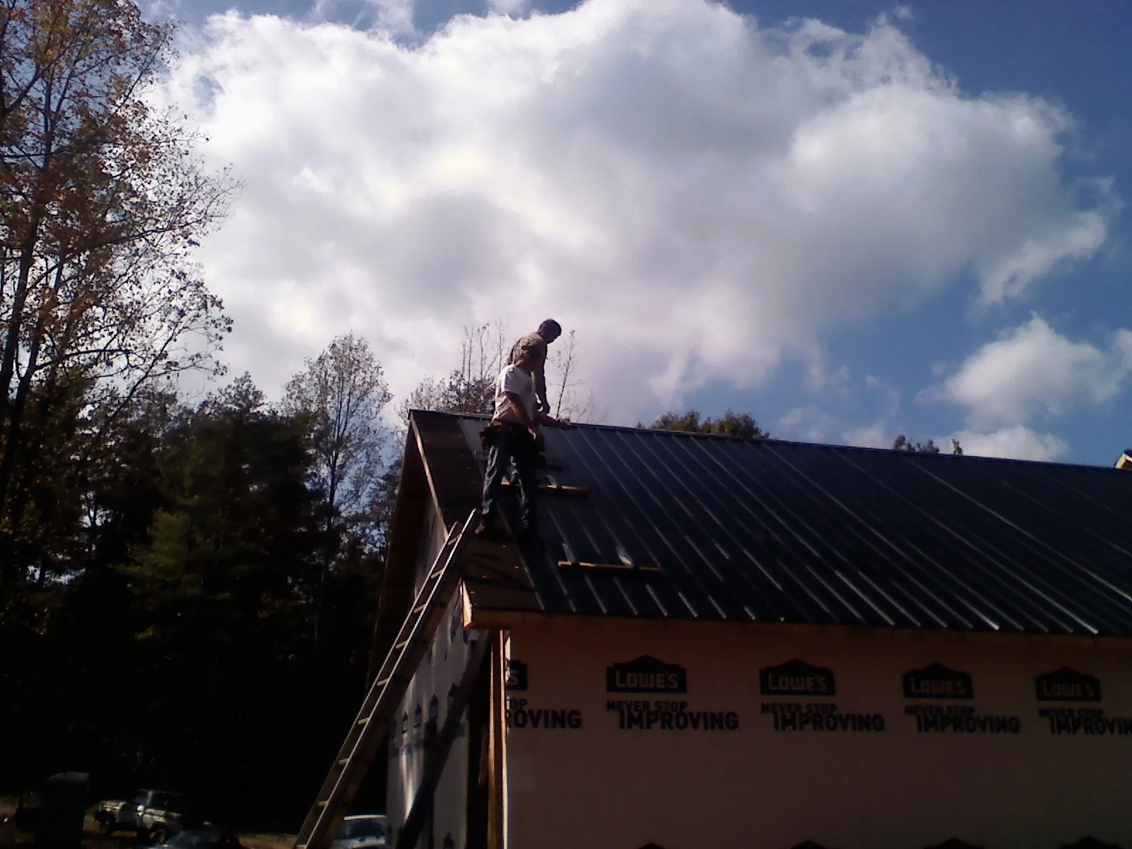 Roofer fastening dark metal panels high against a cloudy sky, from a Roof Inspection job in Yerington