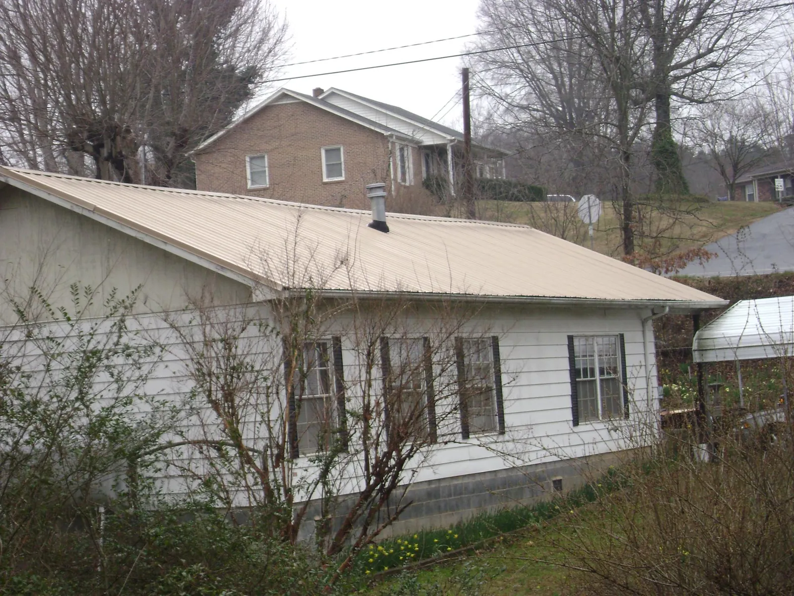 Tan metal roof on a white sided house set into a hillside — Commercial Roofing by Roofing Brothers in Yerington